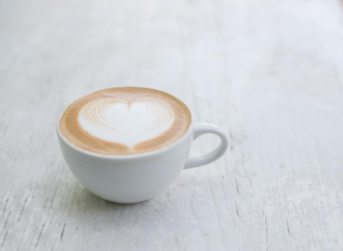 xícara de café com leite com formato de coração na mesa branca foto