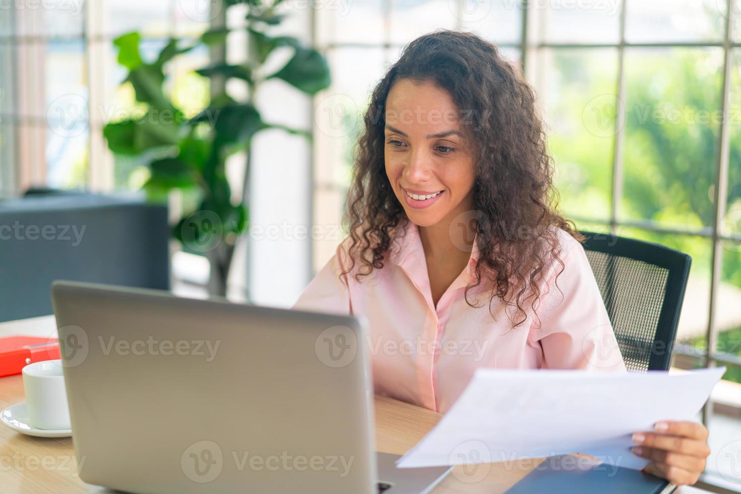 mulher latina trabalhando com laptop e papel na área de trabalho foto