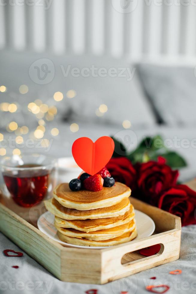 café da manhã ou brunch do dia dos namorados. panquecas caseiras com bagas, xícara de chá e rosas vermelhas. copie o espaço foto