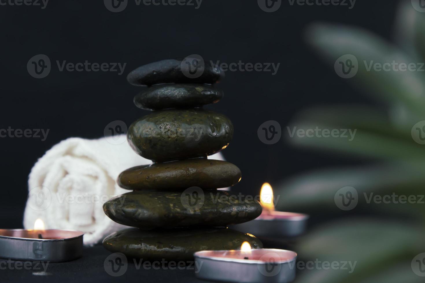 pedras quentes pretas sobre fundo escuro de madeira, camadas de configuração de massagem com pedras quentes iluminadas pela luz de velas. terapia de massagem para uma pessoa com luz de velas para relaxar, conceito de ioga. foto