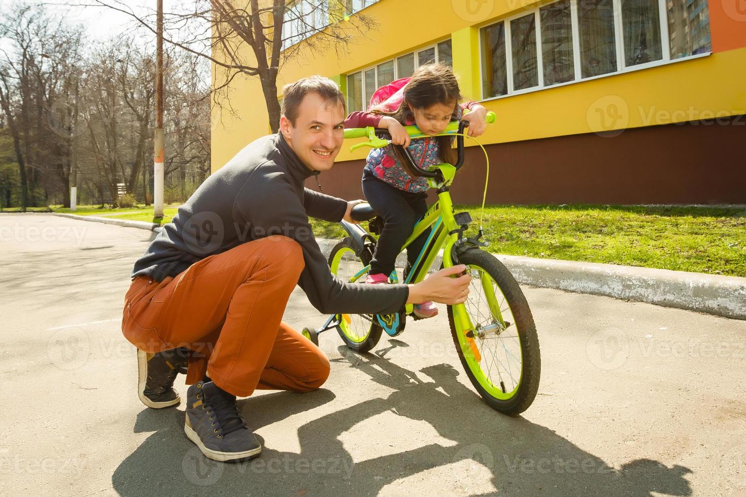 pai feliz ensinando sua filha a andar de bicicleta. criança aprendendo a andar de bicicleta. atividades familiares no verão. foto