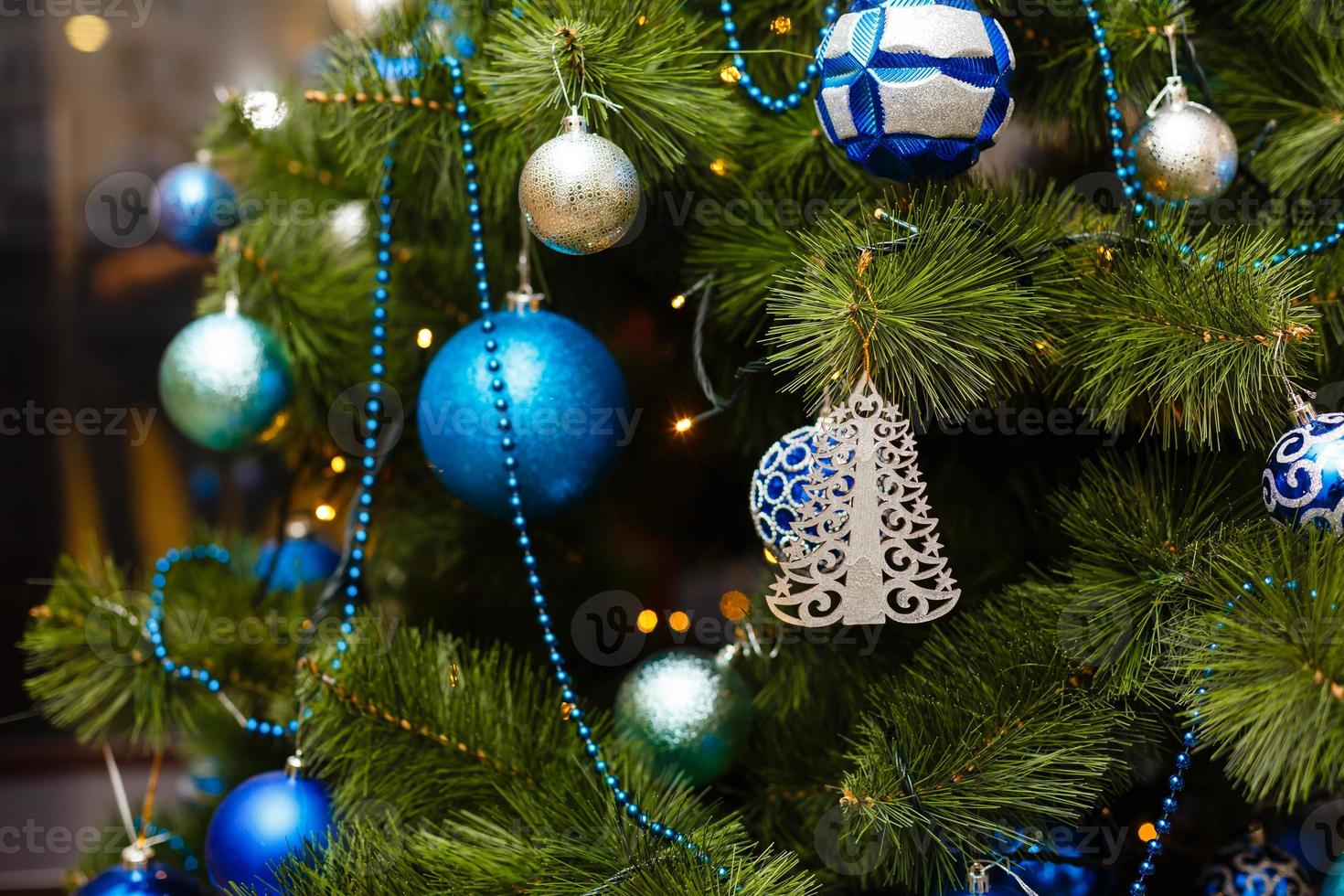 enfeite de bola azul pendurado na folha de pinheiro para decoração de árvore de natal com borrão de luz colorida foto