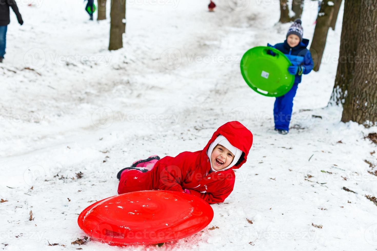 menina muito sorridente em seu traje de esqui deslizando por uma pequena colina coberta de neve com seu trenó foto