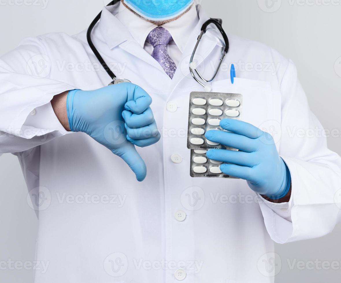 O terapeuta médico adulto está vestido com um casaco uniforme branco e luvas estéreis azuis está de pé e segurando uma pilha de comprimidos foto