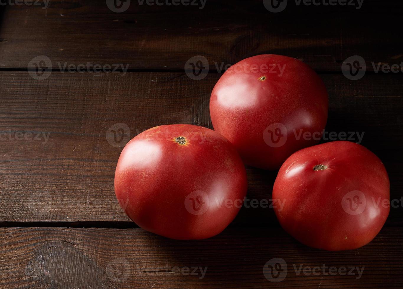 três tomates vermelhos maduros em um fundo de madeira marrom foto