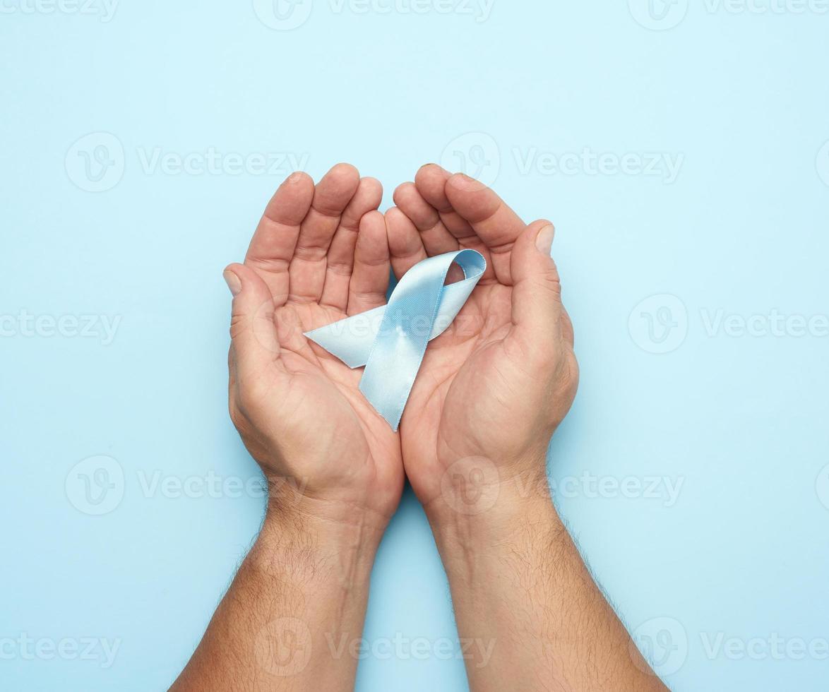 a mão masculina segura a fita de seda azul na forma de um laço em um fundo azul foto