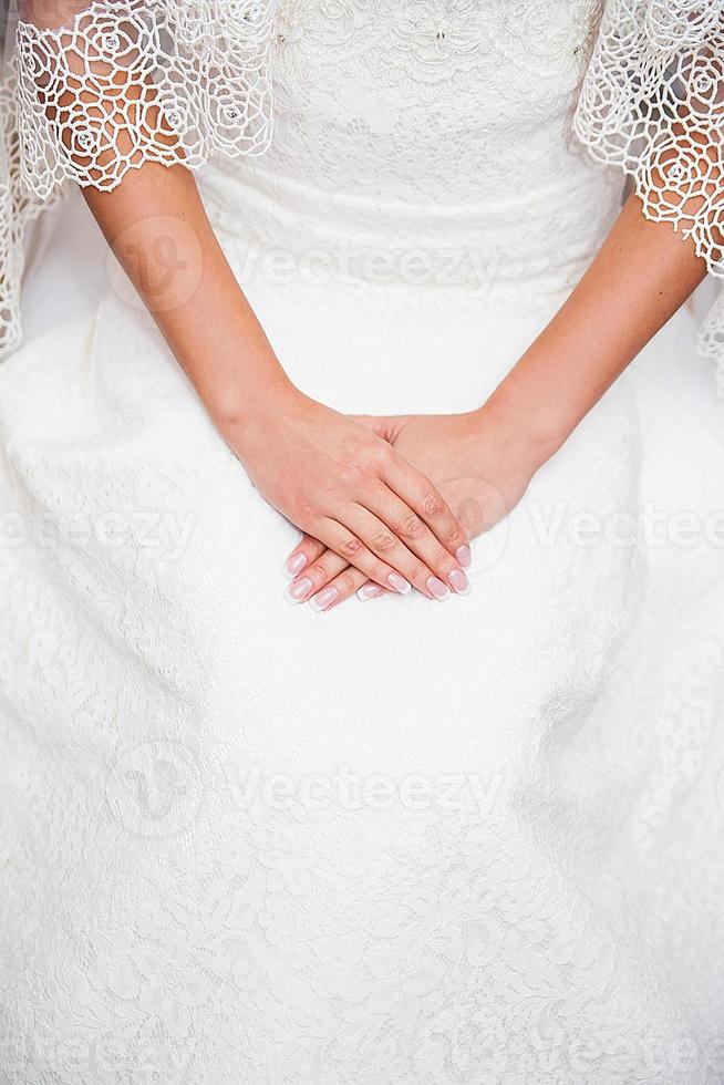 mão da noiva no vestido de noiva com uma bela manicure foto