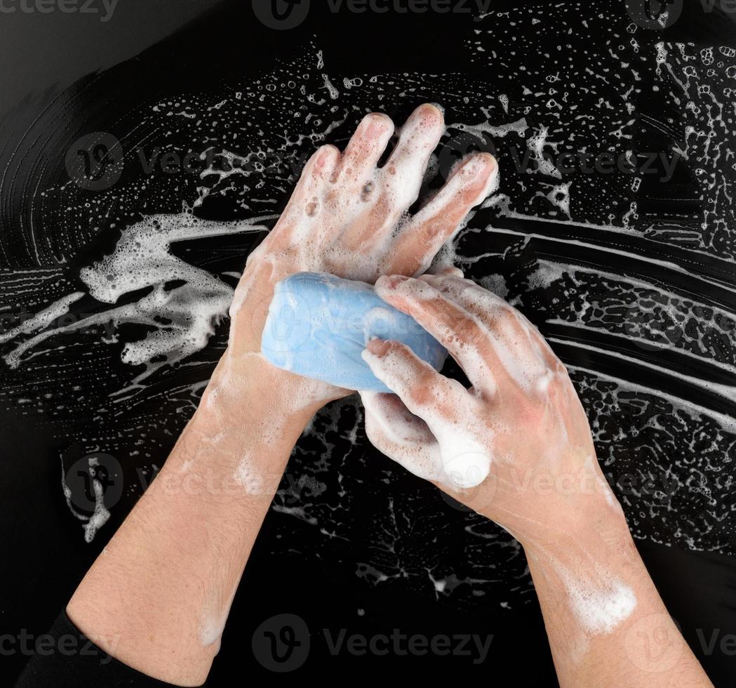 processo de lavagem das mãos com sabão azul, partes do corpo em espuma branca sobre fundo preto foto