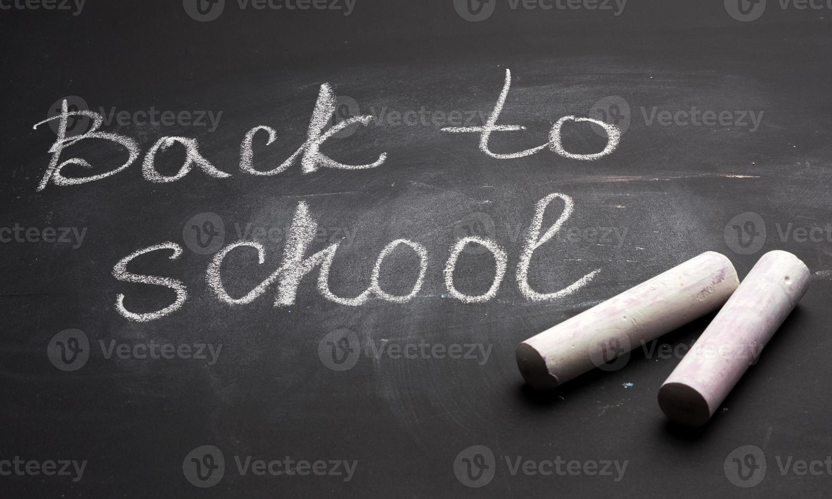 letras de volta à escola em giz branco em um conselho escolar preto e um pedaço de giz foto