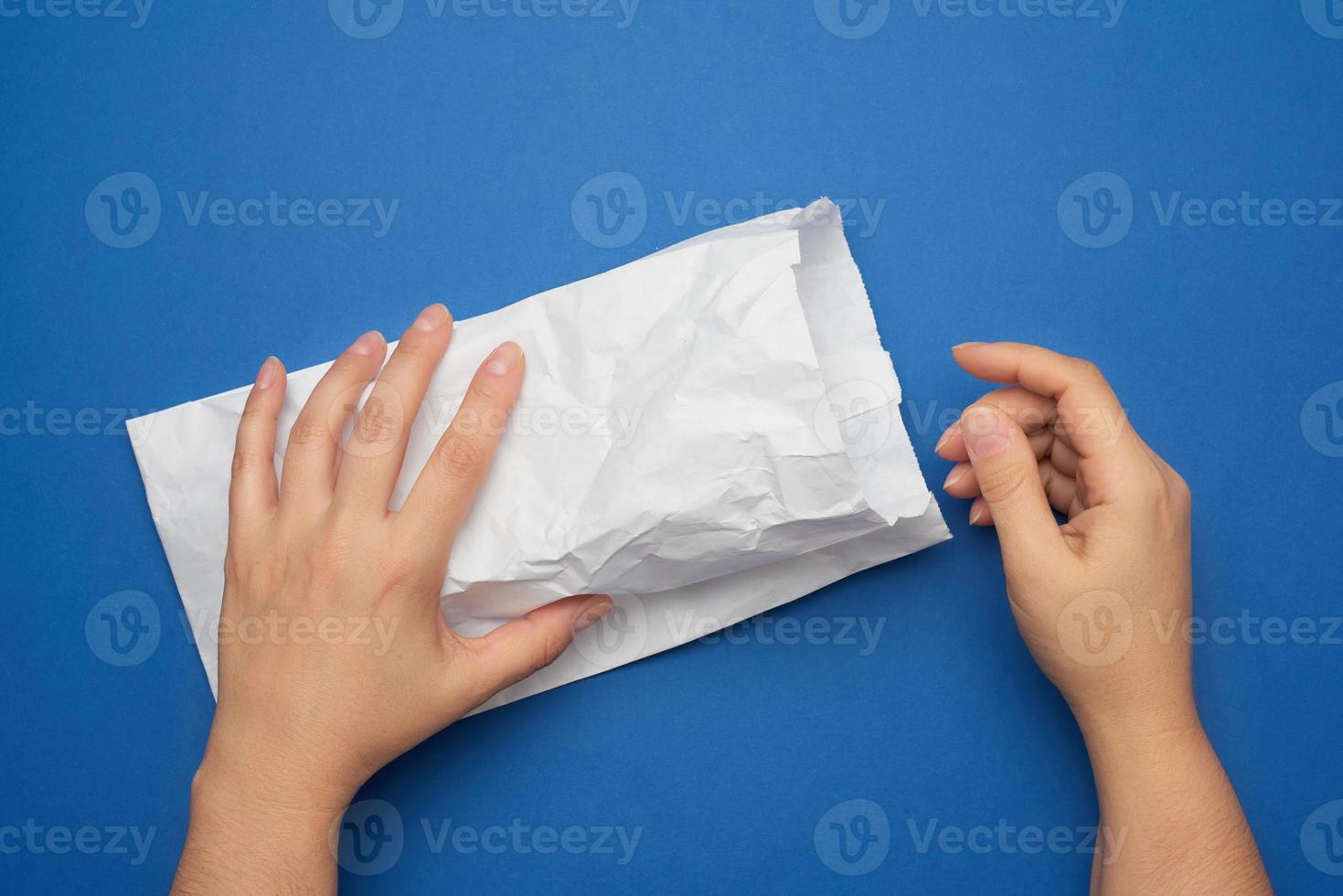 duas mãos femininas seguram um saco de papel branco sobre um fundo azul foto