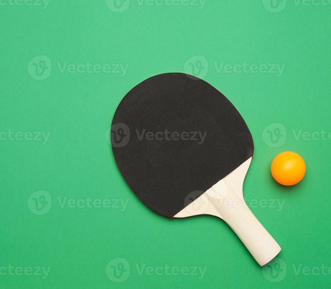 raquete de madeira preta e bola de tênis de mesa laranja de plástico, vista superior foto
