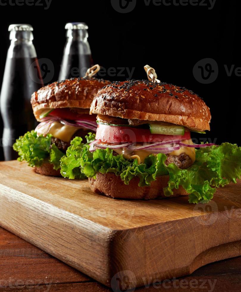 delicioso hambúrguer com costeleta de carne frita e cebola. pão de farinha de trigo branco crocante com sementes de gergelim. fast-food em uma placa de madeira foto