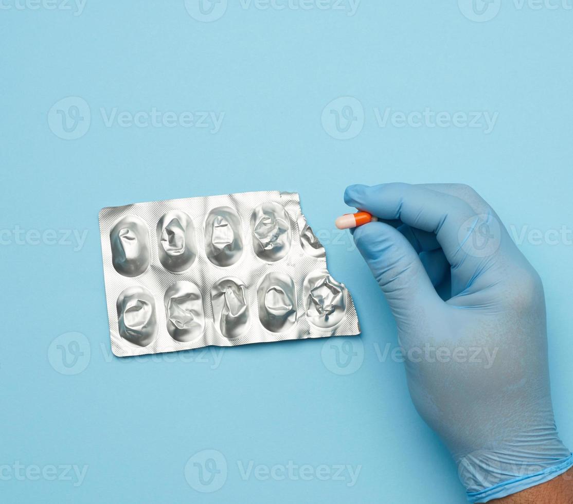 mão masculina em uma luva de borracha estéril azul segura uma pilha de comprimidos em um blister foto