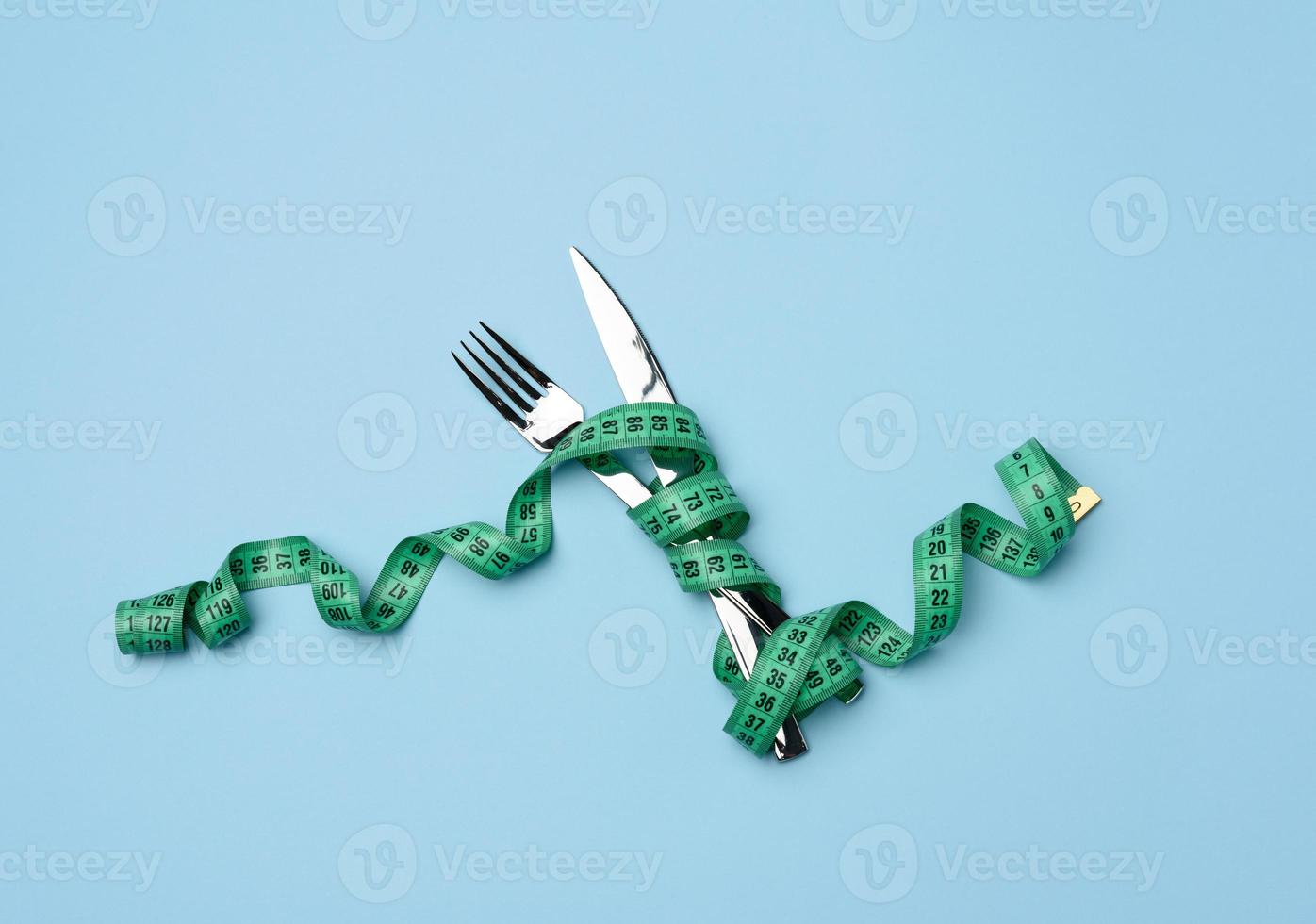 garfo e faca embrulhados em fita métrica verde sobre fundo azul foto