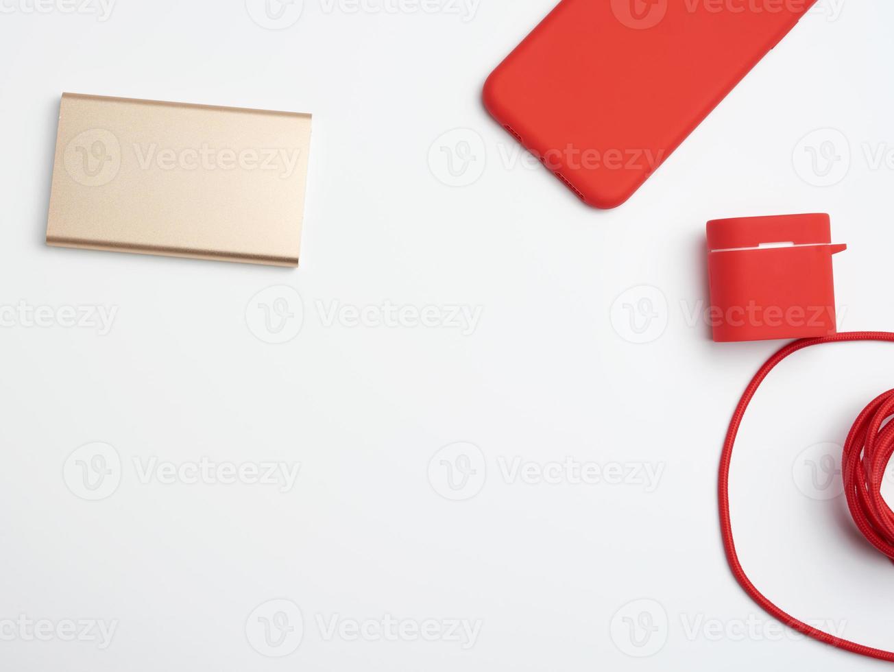 banco de energia dourado, smartphone vermelho e cabo em trança têxtil em um fundo branco foto