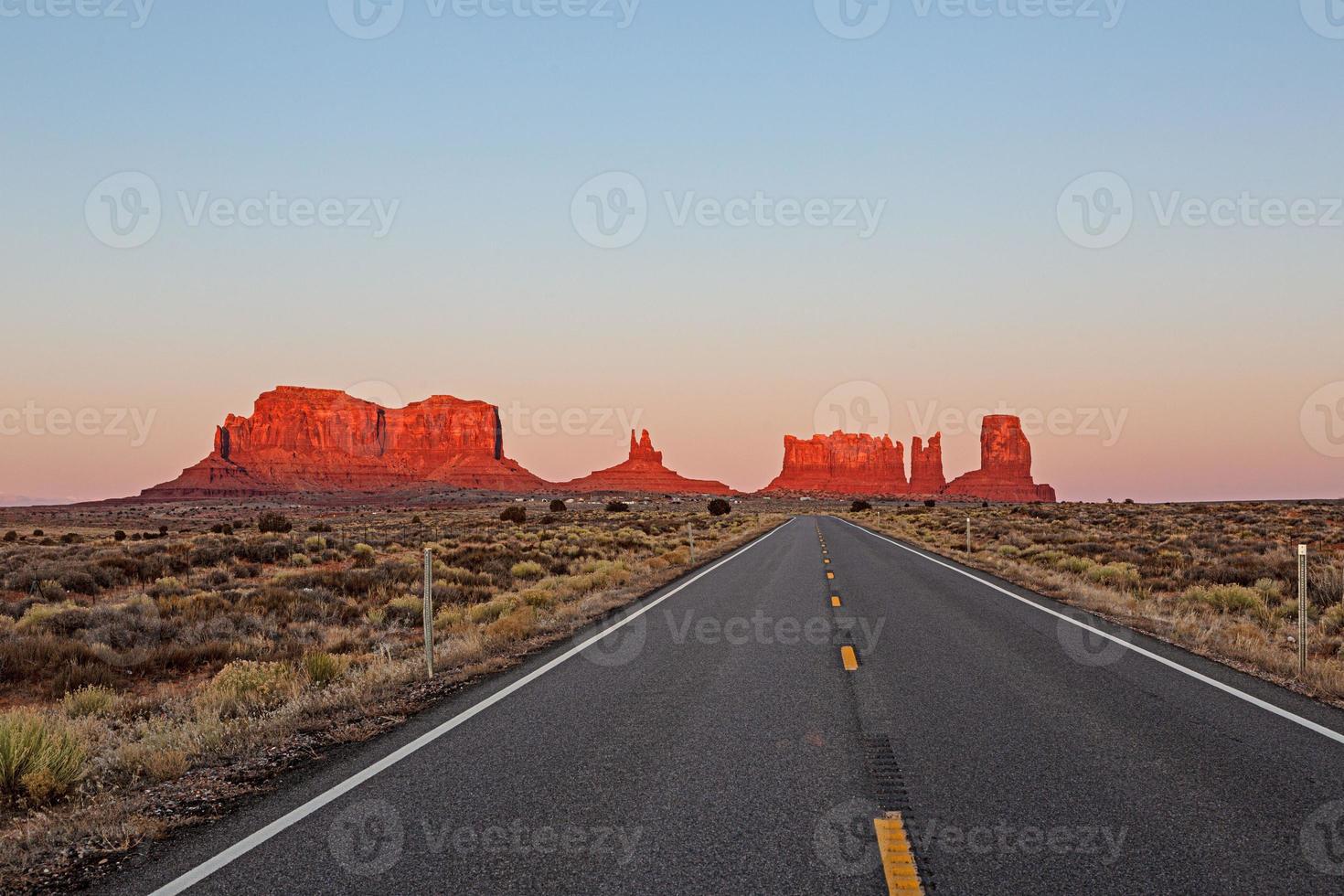 estrada reta leva diretamente ao vermelho ao sol da tarde brilhando na formação rochosa no parque nacional de monumentos em utah foto