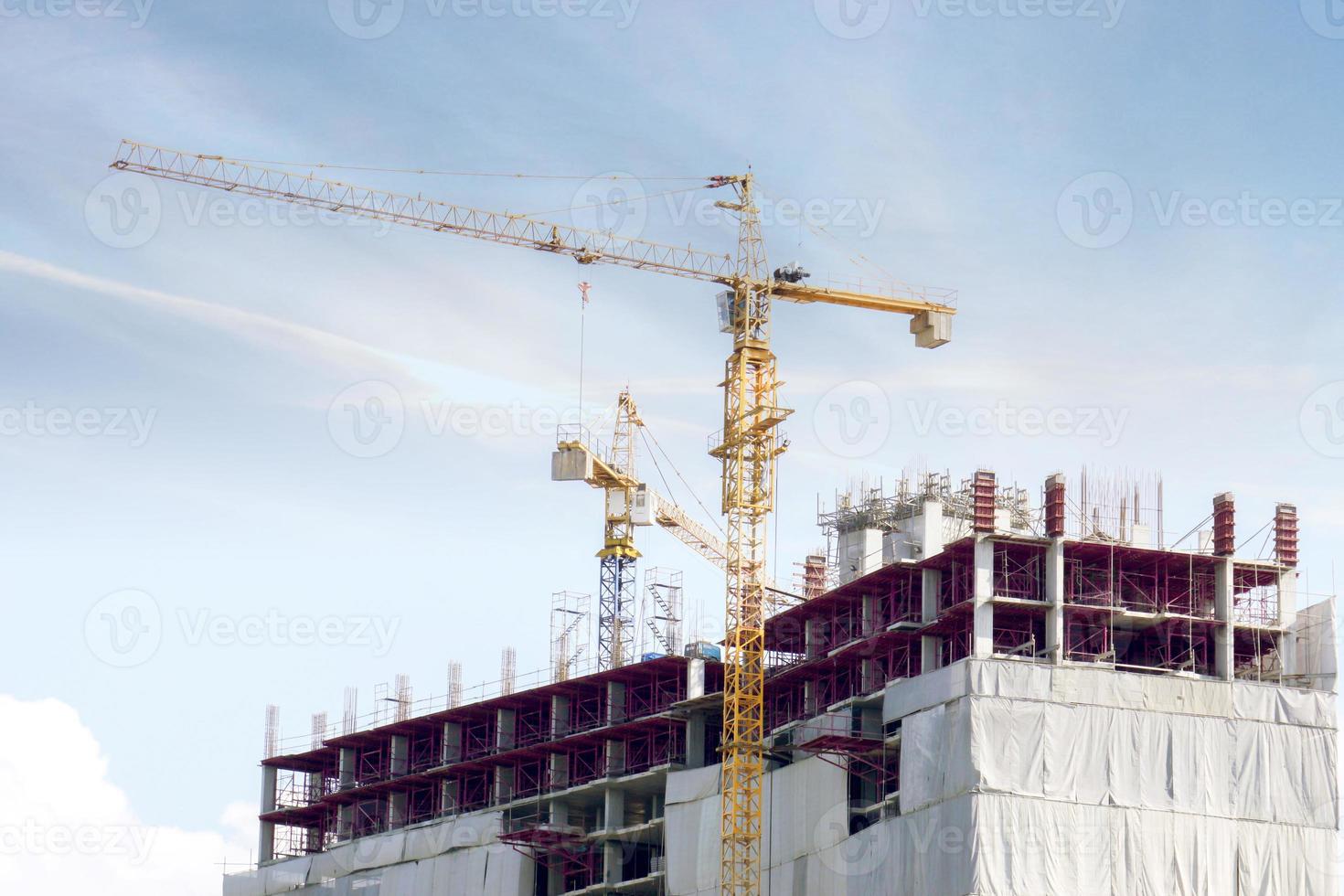 edifício em construção com guindastes trabalhando para mover materiais de construção sob o céu azul e a nuvem de seda. foto