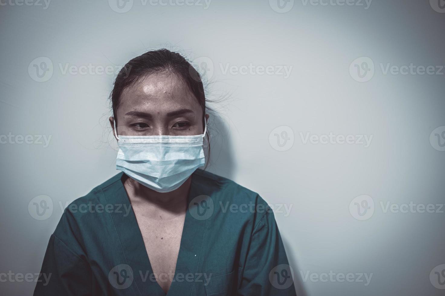 Enfermeira asiática deprimida cansada usa máscara facial uniforme azul senta-se no chão do hospital, jovem médica estressada pelo trabalho duro foto