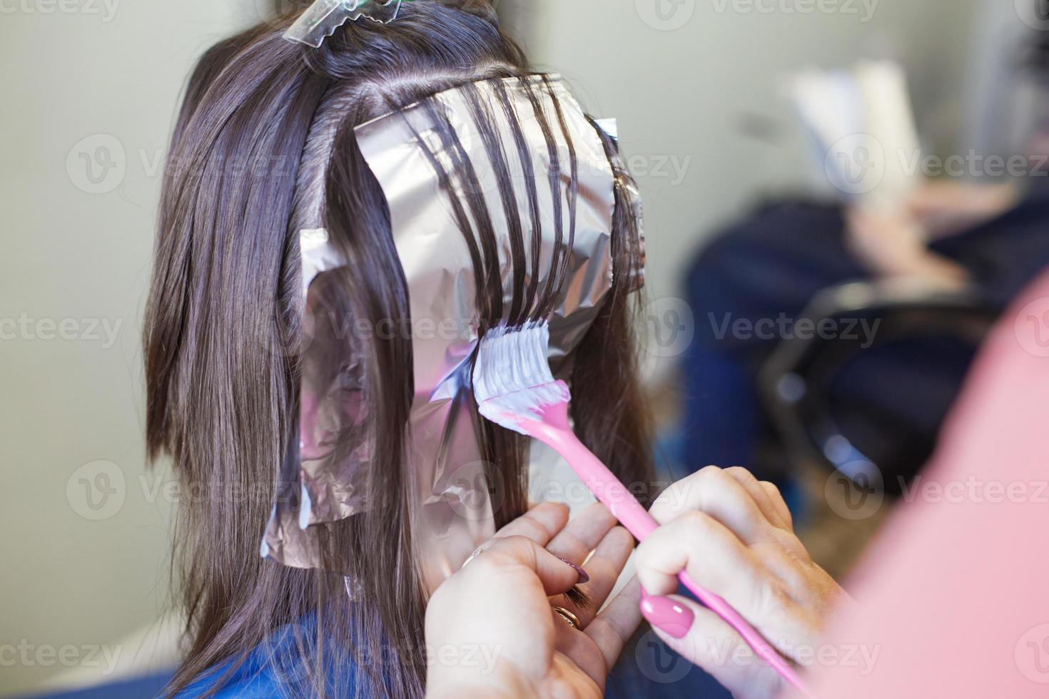 o cabeleireiro pinta o cabelo de uma mulher morena no salão de beleza. foto