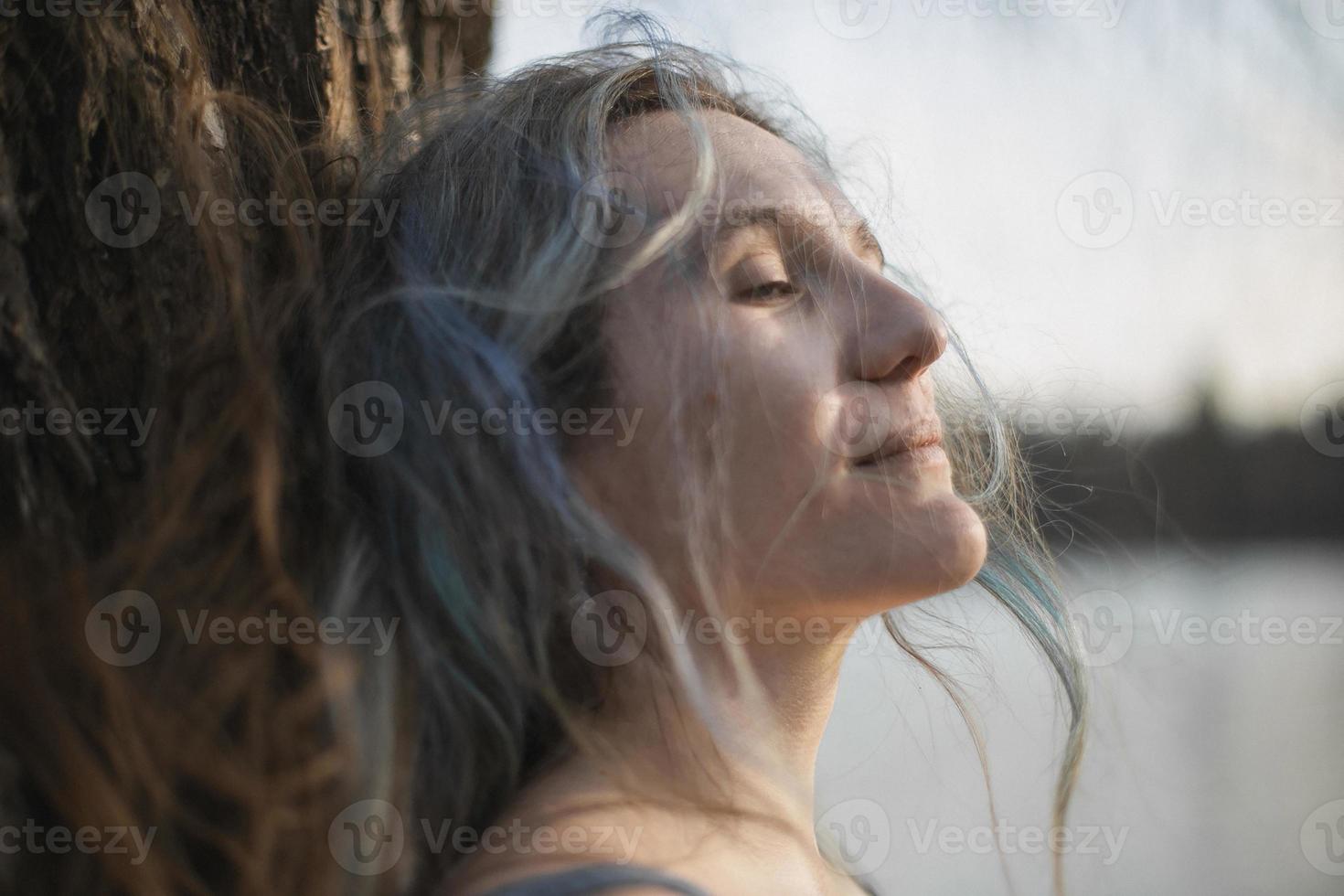close-up mulher de cabelos grisalhos com os olhos semicerrados encostado na foto do retrato de árvore