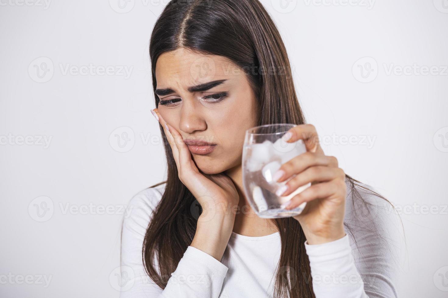 jovem com dentes sensíveis e mão segurando um copo de água fria com gelo. conceito de saúde. mulher bebendo bebida gelada, copo cheio de cubos de gelo e sente dor de dente, dor foto