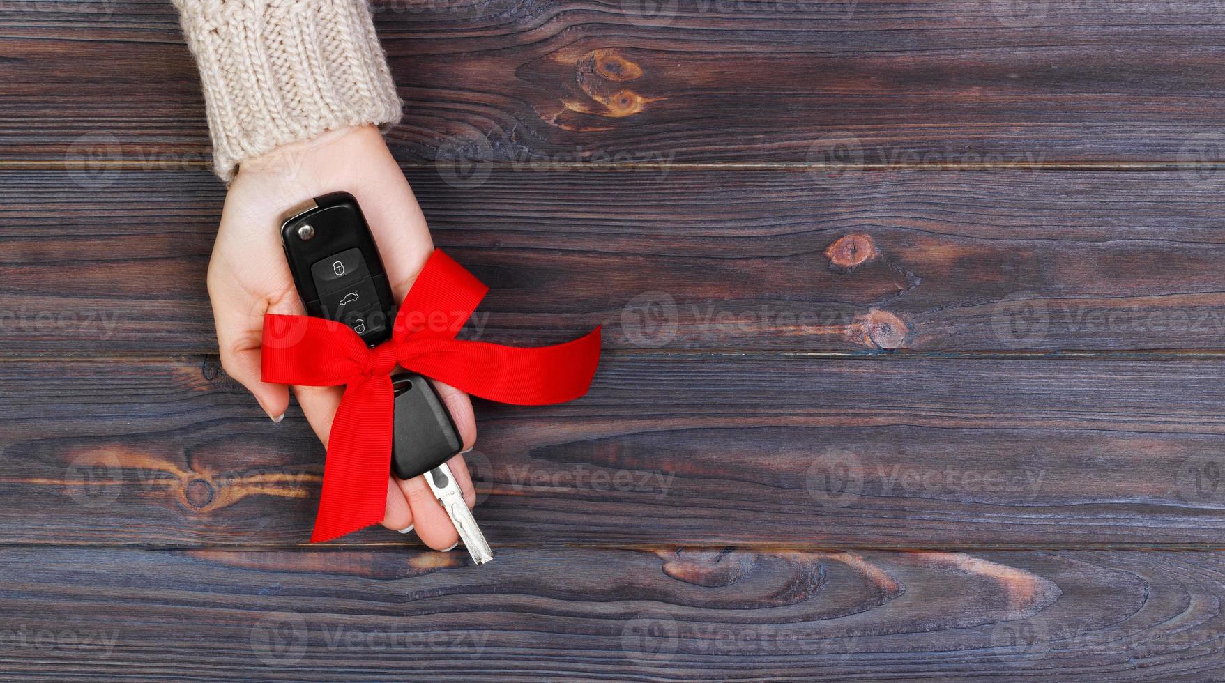 mão de mulher segura a chave do carro com laço vermelho. dando um carro como um banner de presente foto