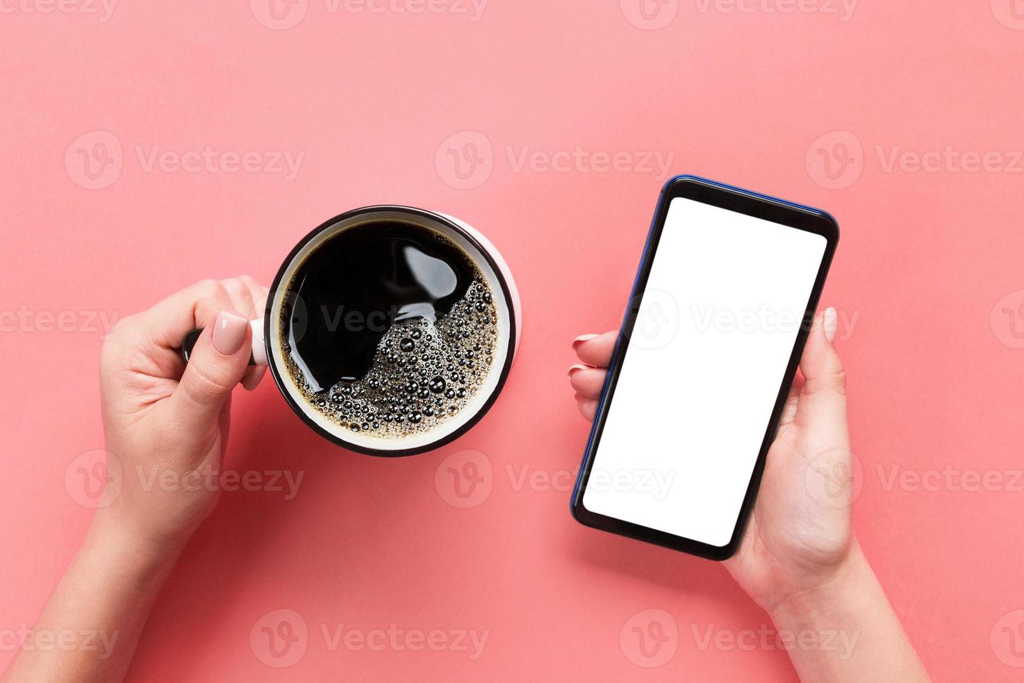 mãos femininas segurando um celular preto com tela branca em branco e caneca de café. imagem de maquete com espaço de cópia. vista superior no fundo rosa, configuração plana foto