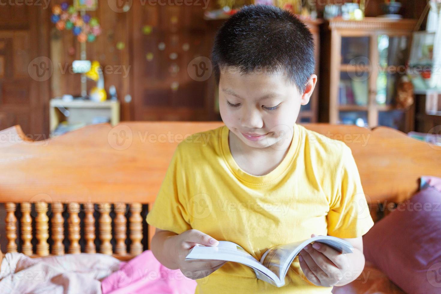 um menino asiático branco com uma covinha na bochecha senta-se alegremente e lê um livro para revisar as lições em casa. foto