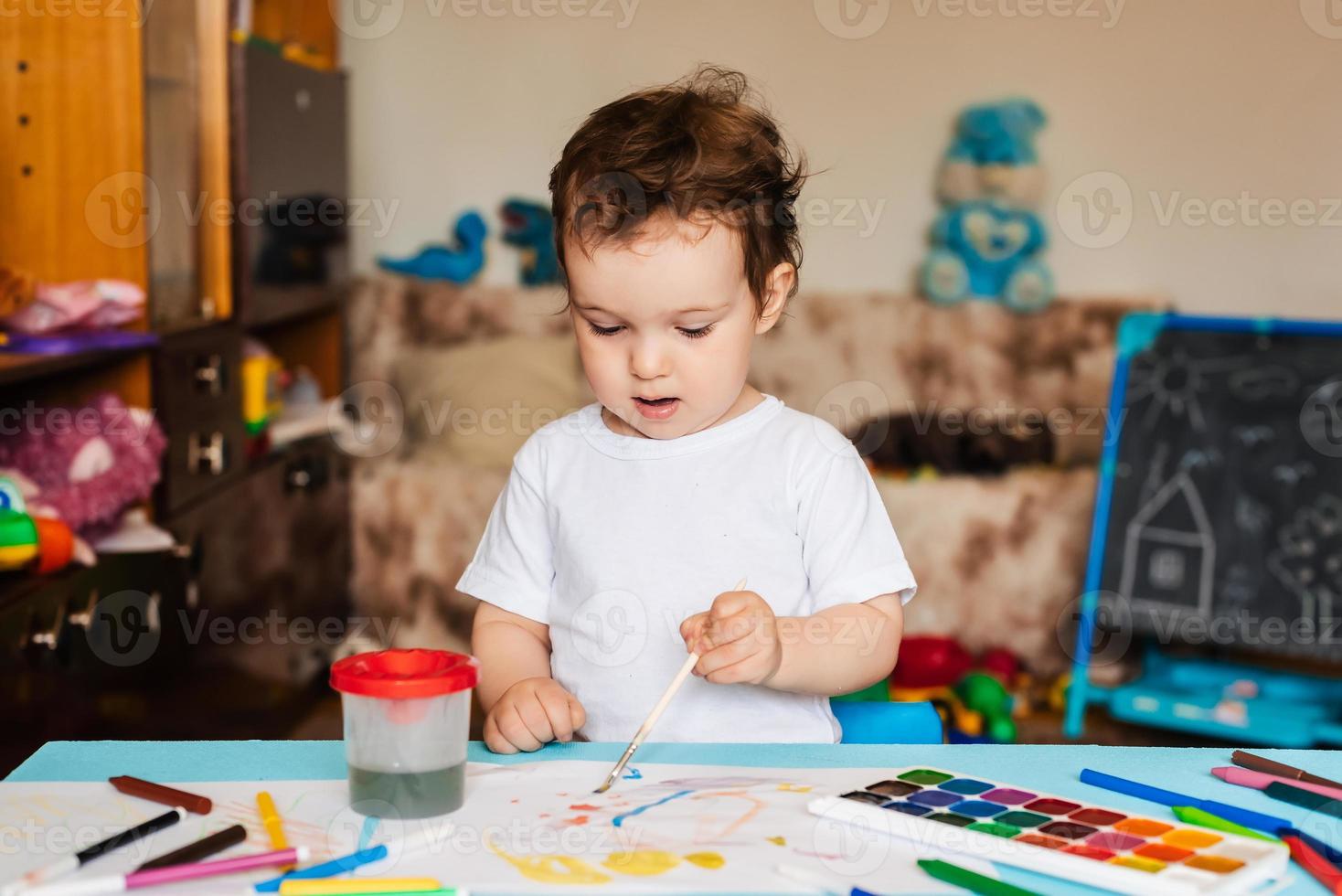 criança alegre feliz desenha com um pincel em um álbum usando tintas multicoloridas foto