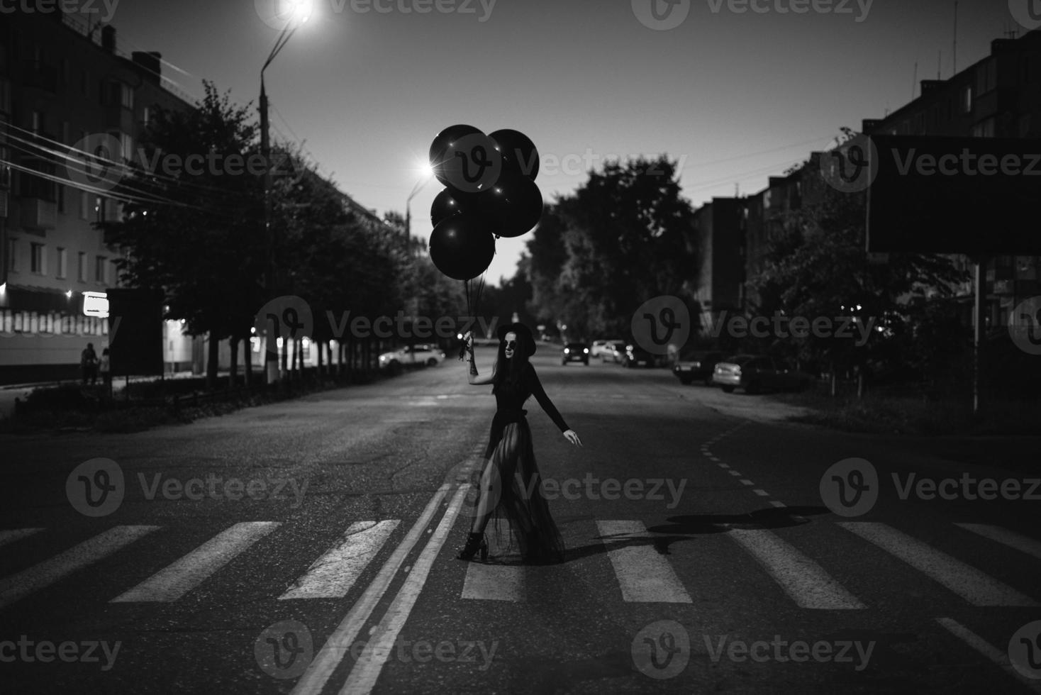 uma garota de preto com balões nas mãos atravessa a rua foto