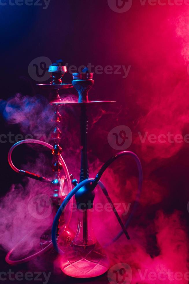 cachimbo de água na moda com uma nuvem de fumaça em um fundo preto com brilho vermelho e azul foto