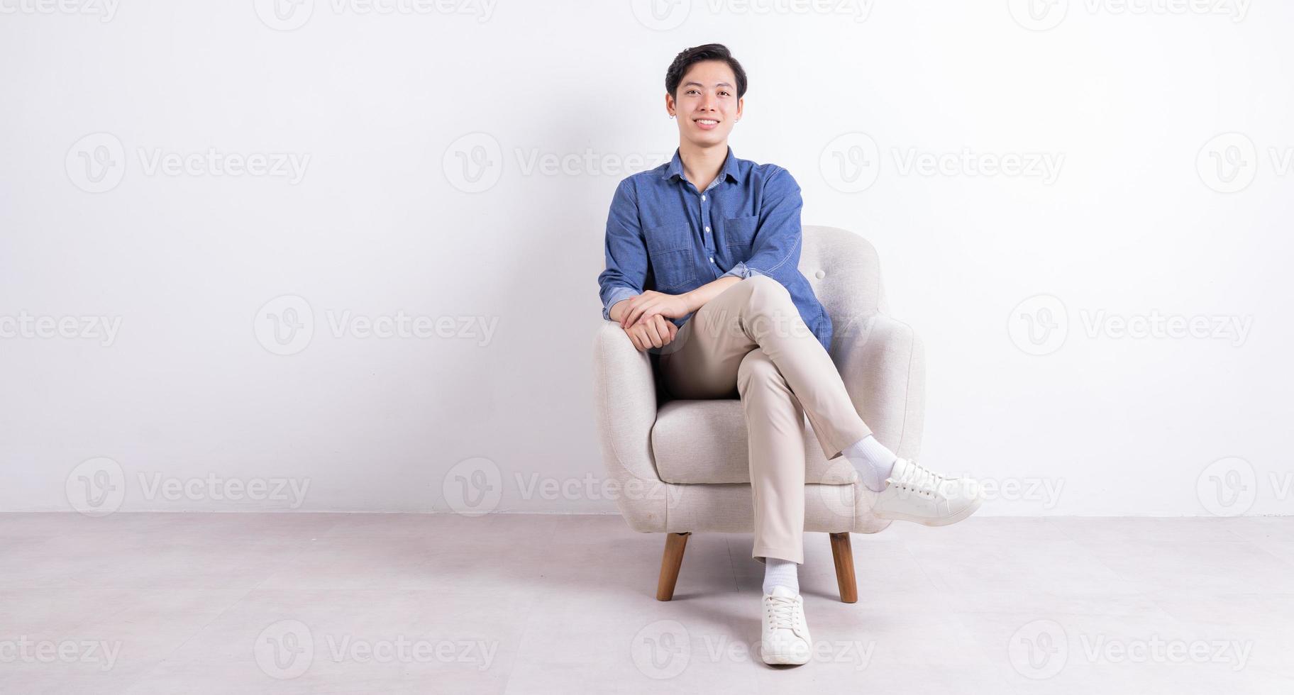 jovem asiático sentado na poltrona em fundo branco foto