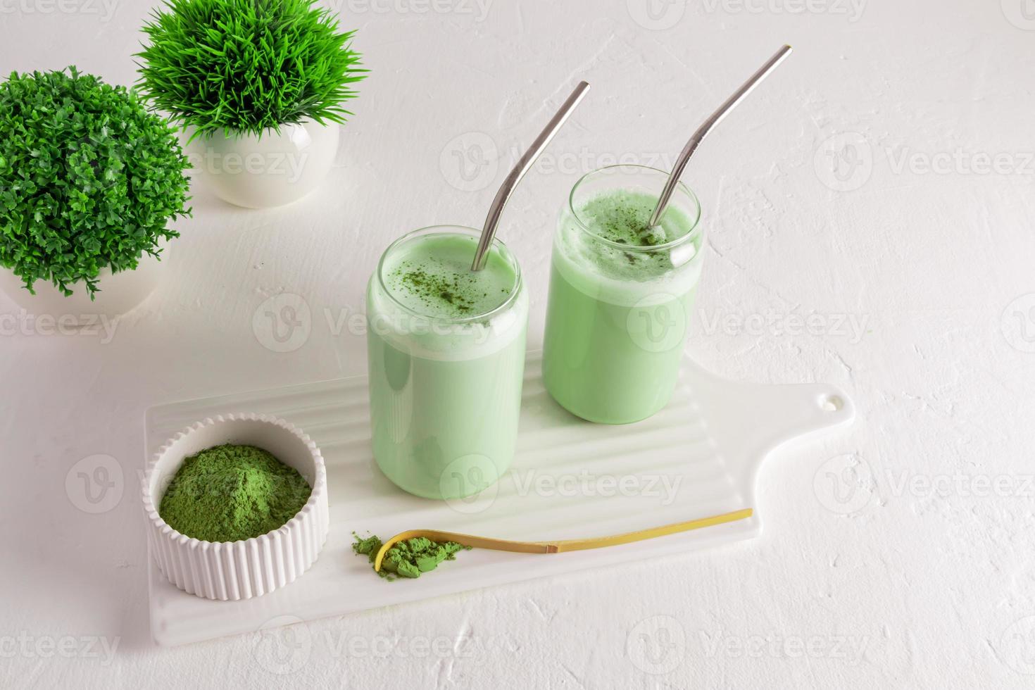 dois copos modernos na forma de uma lata de cerveja com chá verde matcha latte em um quadro branco com uma tigela de matcha verde em pó. bebida orgânica natural. foto