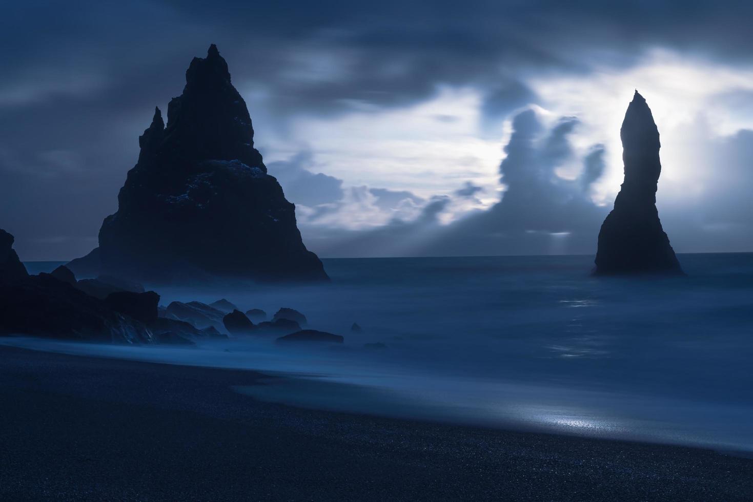 silhuetas de rochas no mar à noite foto