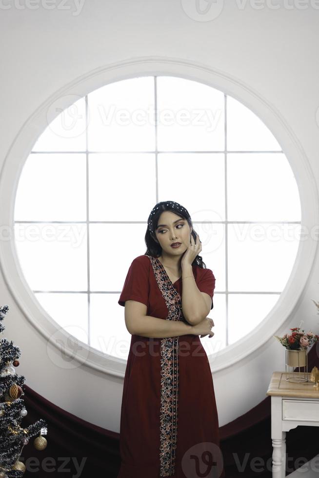 retrato de uma jovem bonita vestindo um vestido vermelho, sorrindo para a câmera, de pé na sala de natal decorada dentro de casa foto