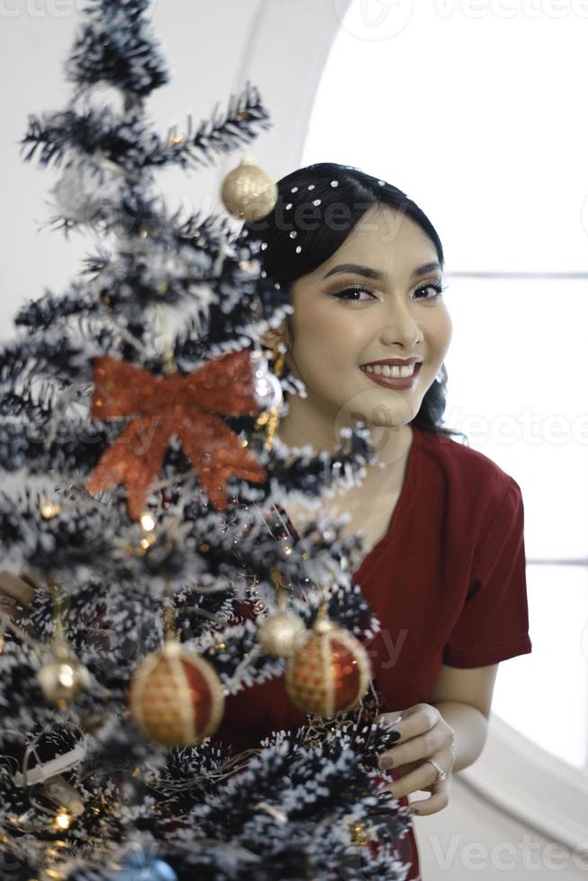 retrato de uma linda jovem decorando a árvore de natal, sorrindo usando vestido vermelho na sala de natal decorada dentro de casa foto