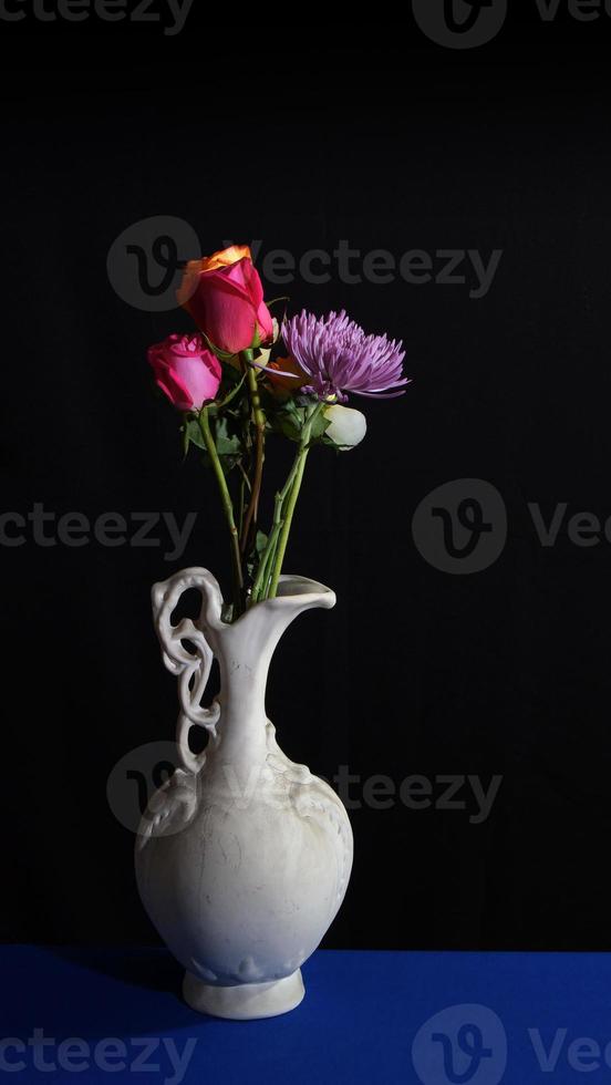 flores em vaso de cerâmica branco velho sobre fundo escuro em formato vertical foto