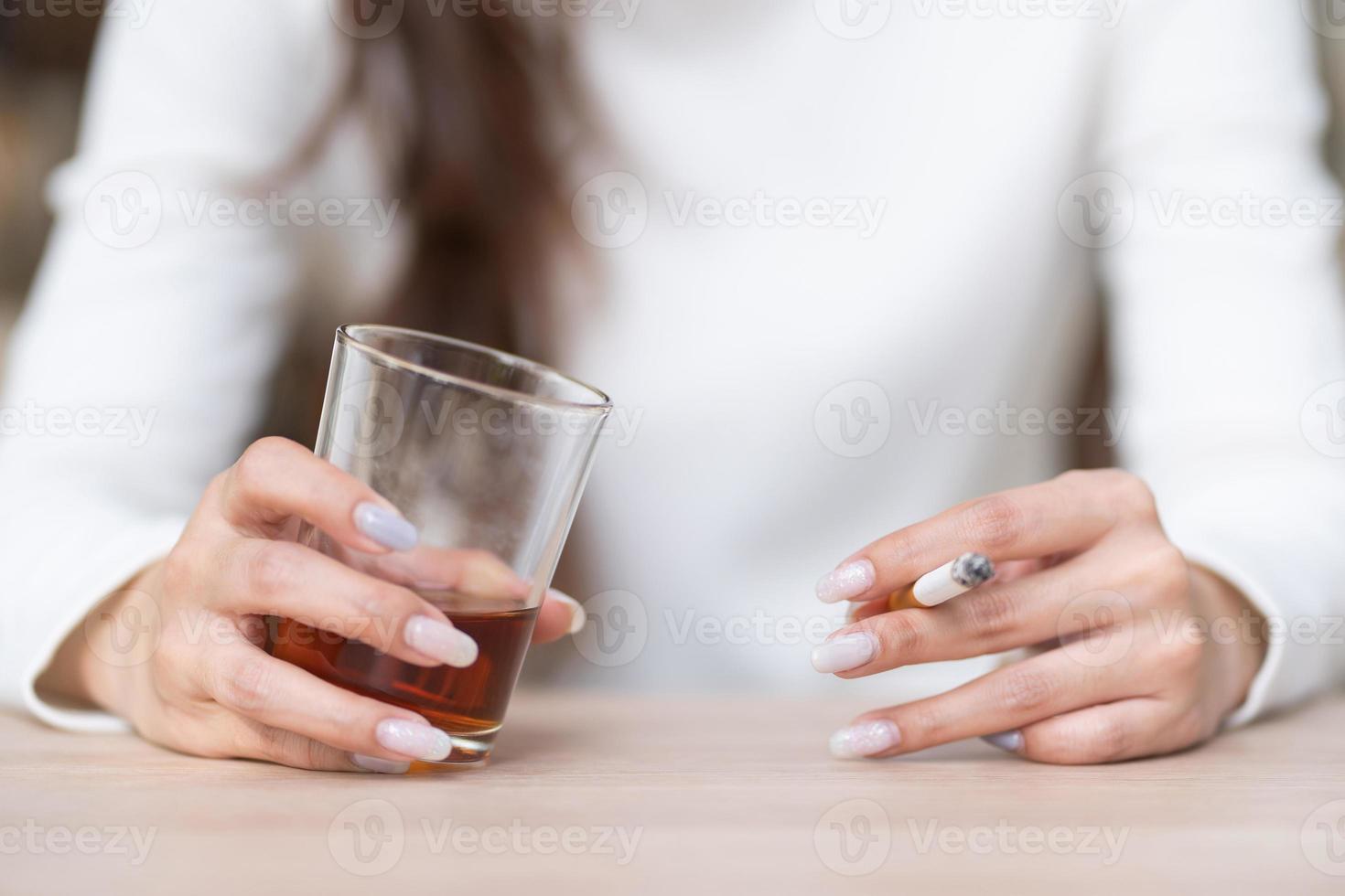 mãos de mulher deprimida bebendo álcool e fumando cigarro sozinho. foto