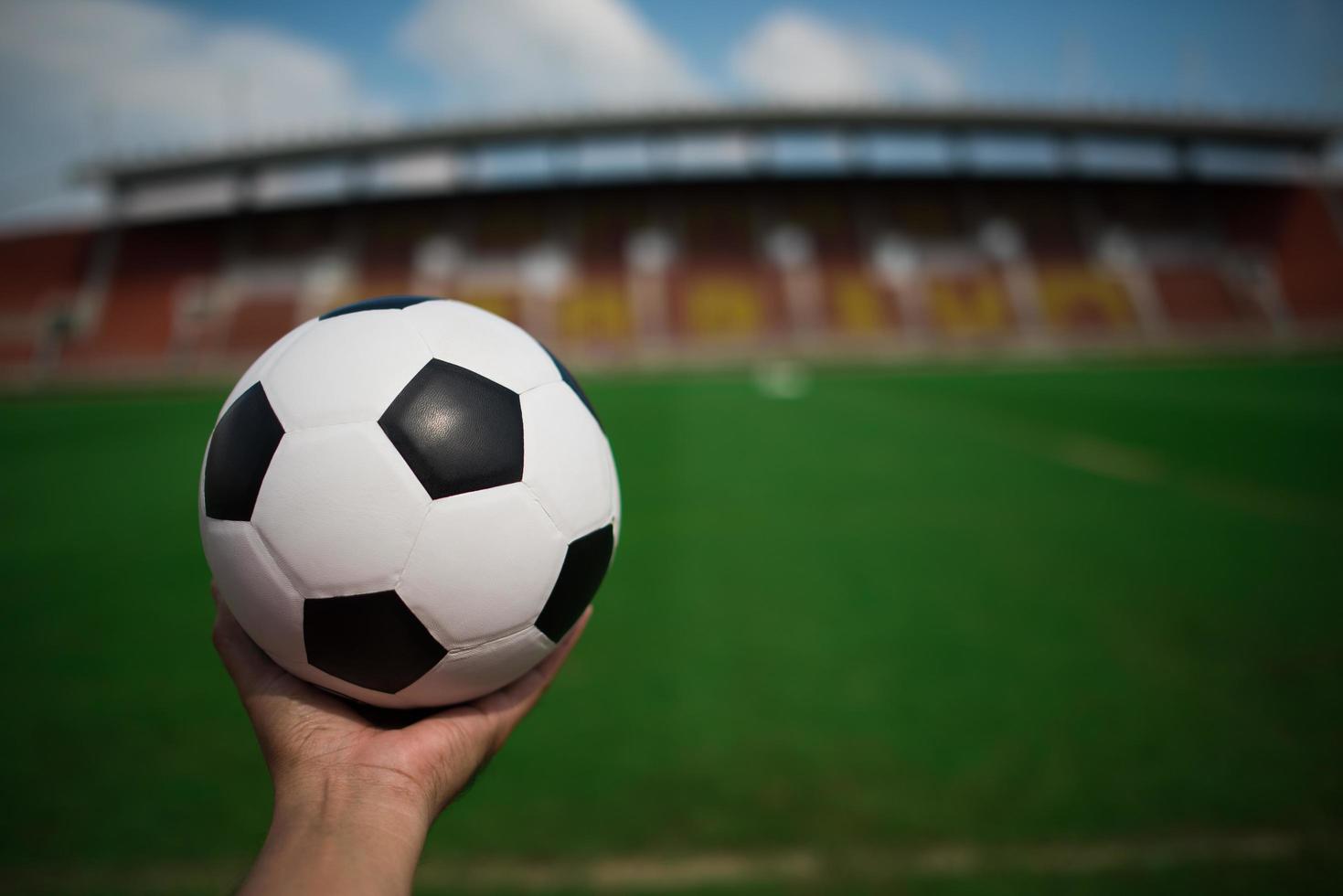 mão segurando uma bola de futebol na grama com o fundo do estádio foto