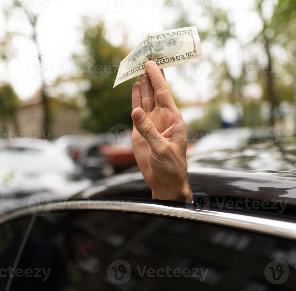 uma mão estendida do carro segura uma nota de 100 dólares. foto