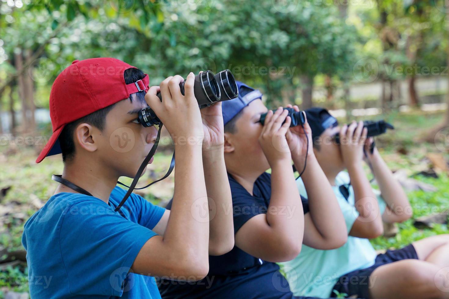 três meninos asiáticos usam binóculos para observar pássaros em uma floresta comunitária própria. o conceito de aprendizagem a partir de fontes de aprendizagem fora da escola. foco no primeiro filho. foto