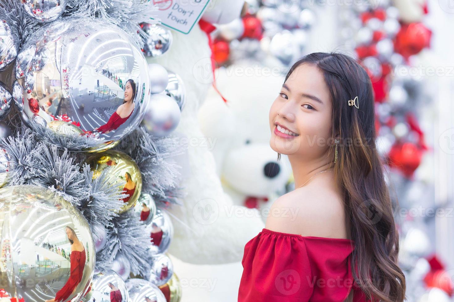 linda garota asiática bonita usa casaco vermelho enquanto olha para a câmera sorrindo alegremente no tema de celebração de natal e ano novo em bokeh de fundo. foto