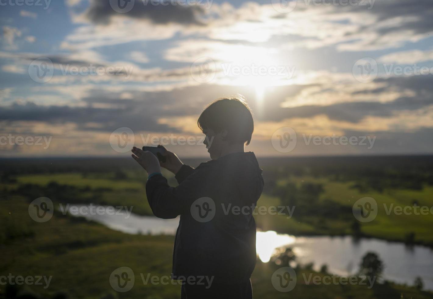 um menino tira fotos em seu telefone de uma incrível paisagem montanhosa com um lago durante o pôr do sol. o menino está observando a natureza. liberdade de estilo de vida.
