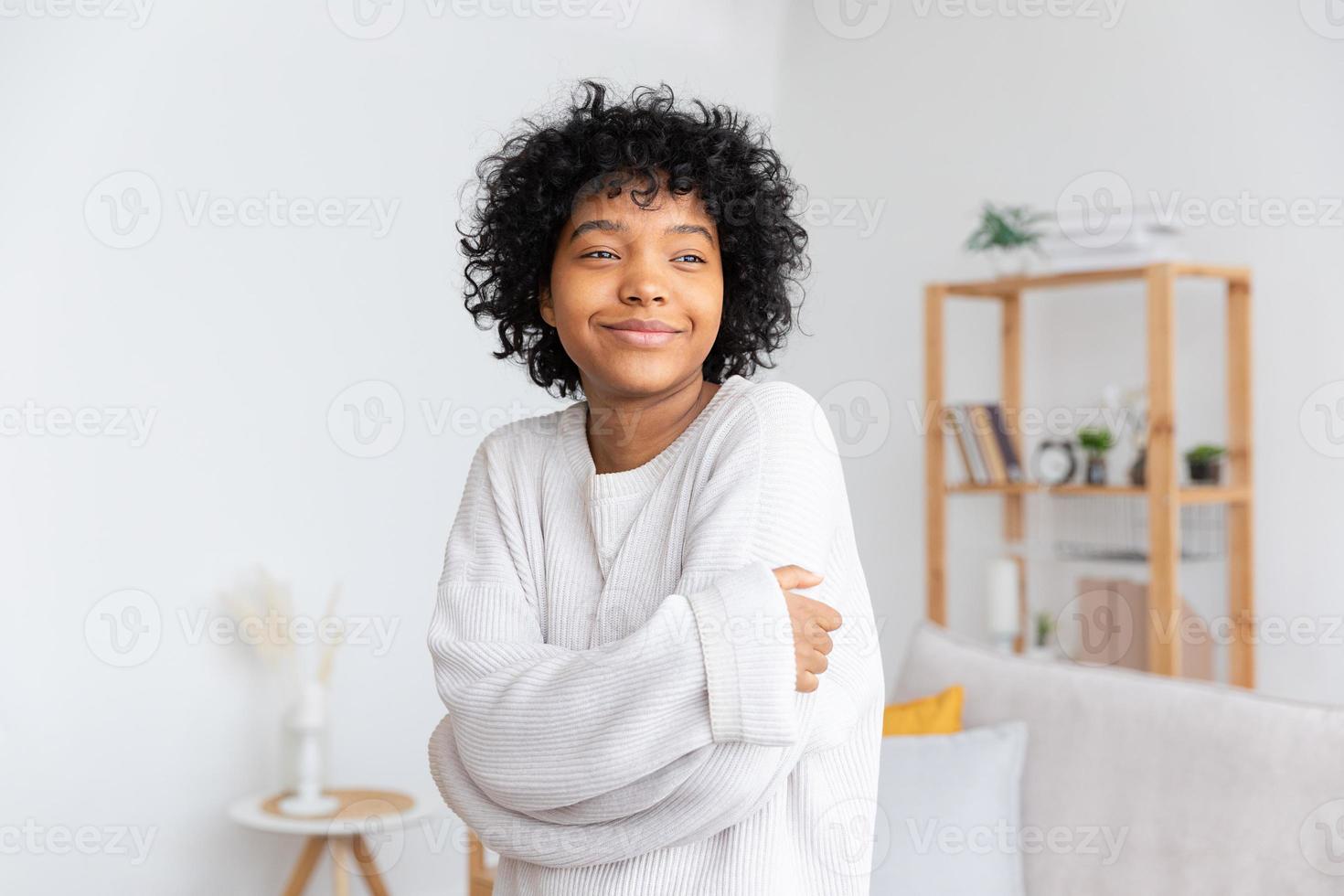 linda garota afro-americana com penteado afro sorrindo em casa interior. jovem africana com cabelos cacheados rindo na sala de estar. liberdade felicidade despreocupado conceito de pessoas felizes. foto