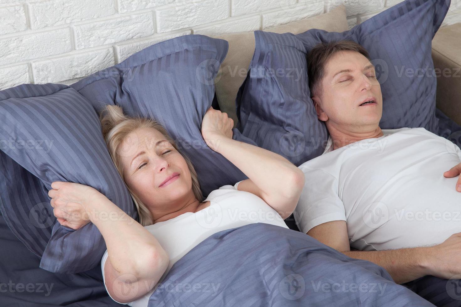 homem roncando. casal na cama, homem roncando e mulher não consegue dormir, cobrindo os ouvidos com travesseiro para o barulho do ronco. casal de meia-idade na cama em casa. foto