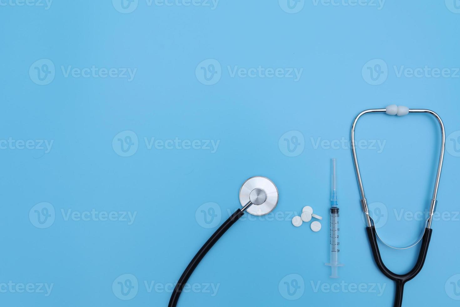 estetoscópio, pílulas brancas e seringa sobre fundo azul. medicamentos. conceito de saúde. copie o espaço foto