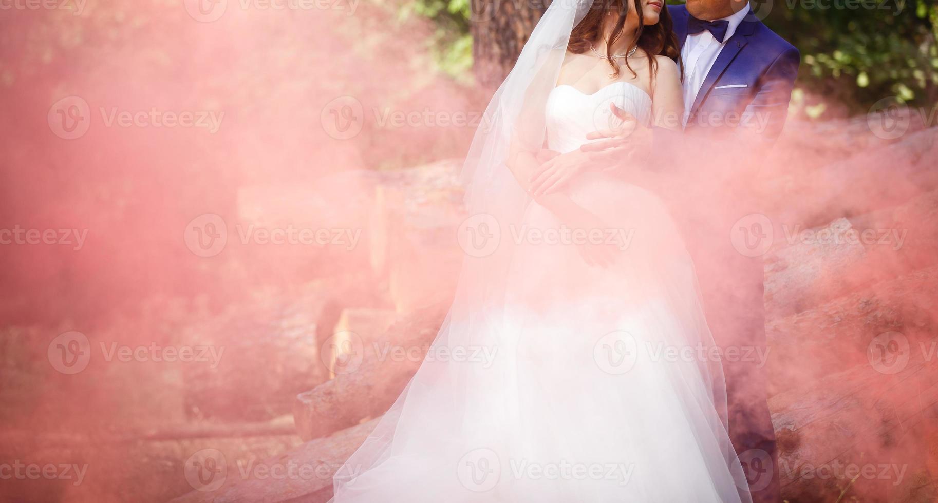 noiva e noivo com a fumaça de cor vermelha no parque de verão foto