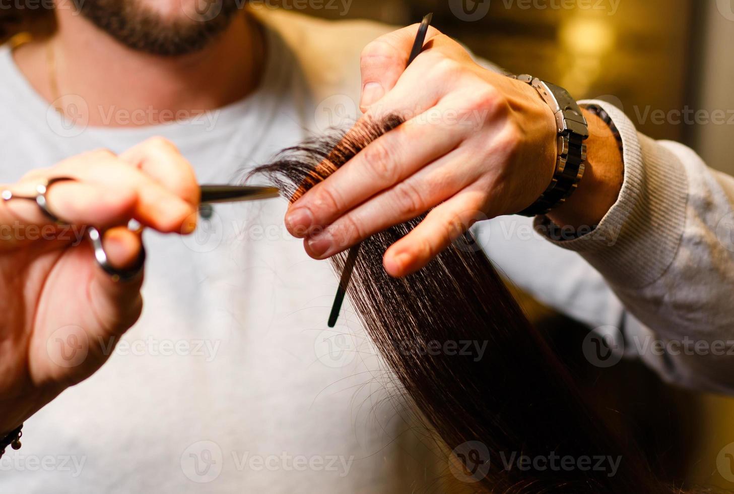 closeup de mãos de cabeleireiro no cabelo saudável da mulher no salão de barbeiro foto