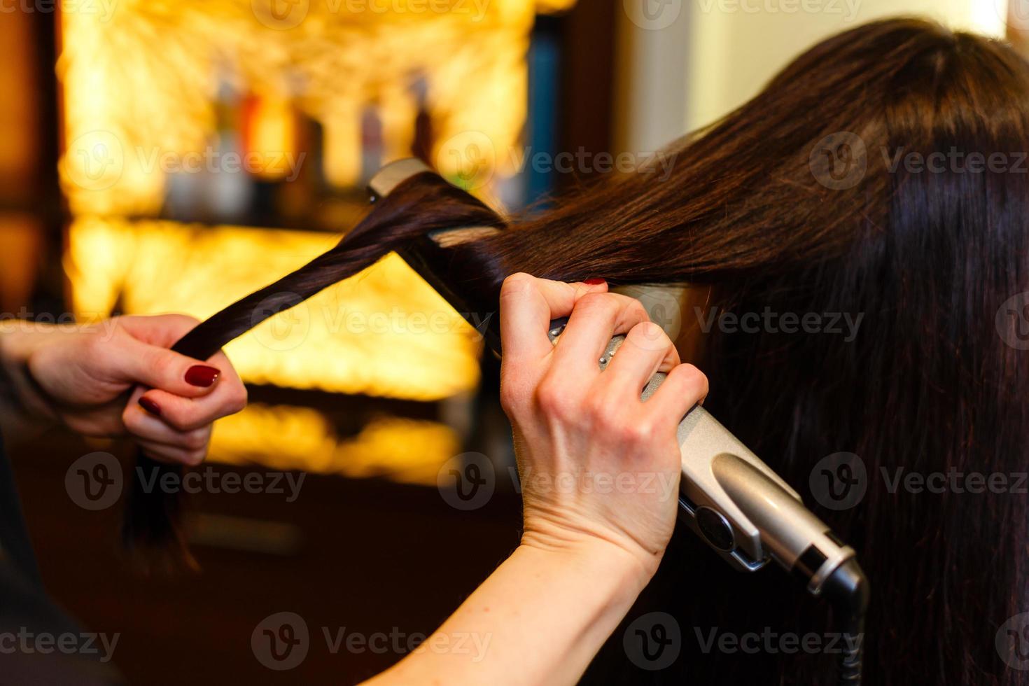 closeup de mãos de cabeleireiro no cabelo saudável da mulher no salão de barbeiro foto