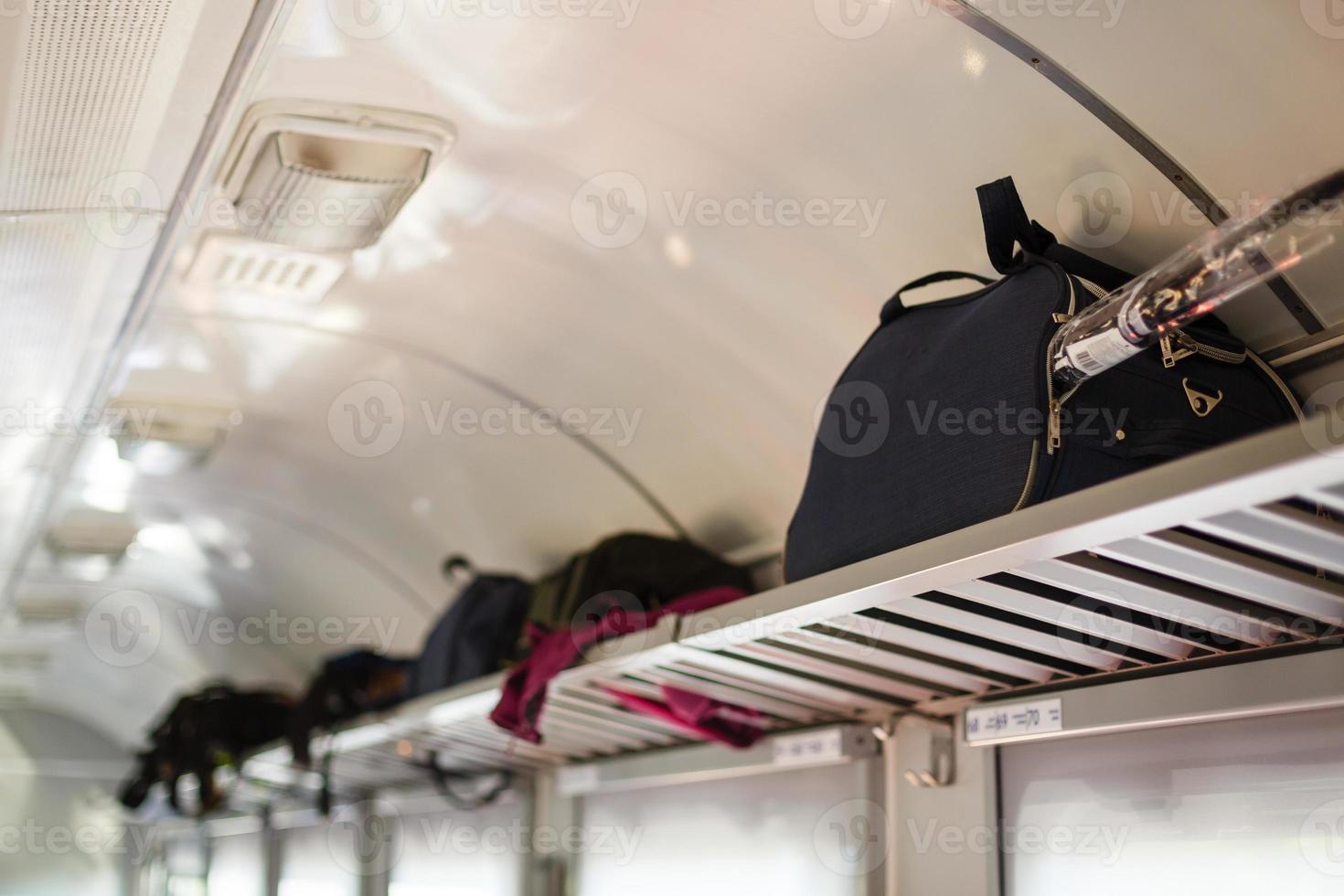 três assentos vazios adjacentes no trem europeu moderno com bagagem na prateleira, orientação vertical do retrato. férias de férias, turismo, viagens, interior de trem moderno ou conceito de transporte ferroviário foto